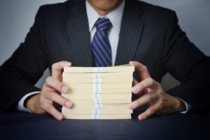 スーツ姿の男性が大量の現金の札束を両手で持っている様子