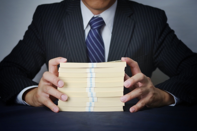 スーツ姿の男性が大量の現金の札束を両手で持っている様子